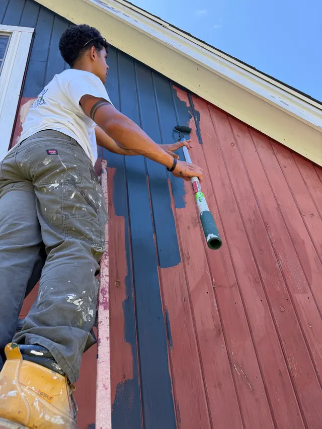 Crew member painting exterior siding from a ladder