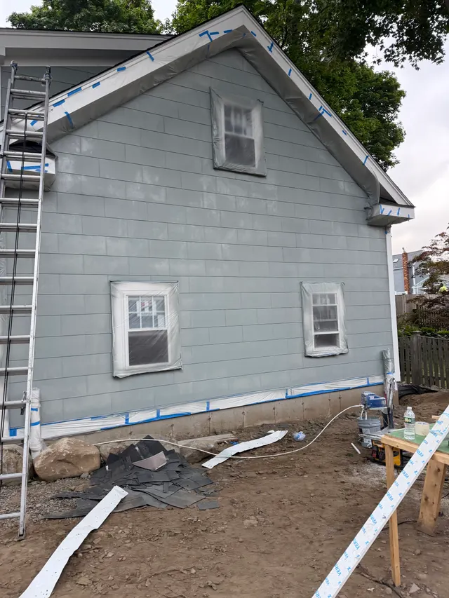 Gray siding, white trim and project equipment beside a garage
